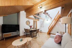 A modern loft-style living space with a wooden ceiling, a flat-screen TV, a dining area with a table and chairs, and a sofa with cushions. - Luxury 2BR Apartment Steps from Old Town Square (Praha)