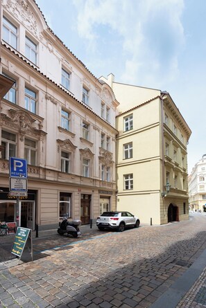 A cobblestone street with a parked scooter and a car, a blue parking sign, and a signboard for a local shop. - Luxury 2BR Apartment Steps from Old Town Square (Praha)