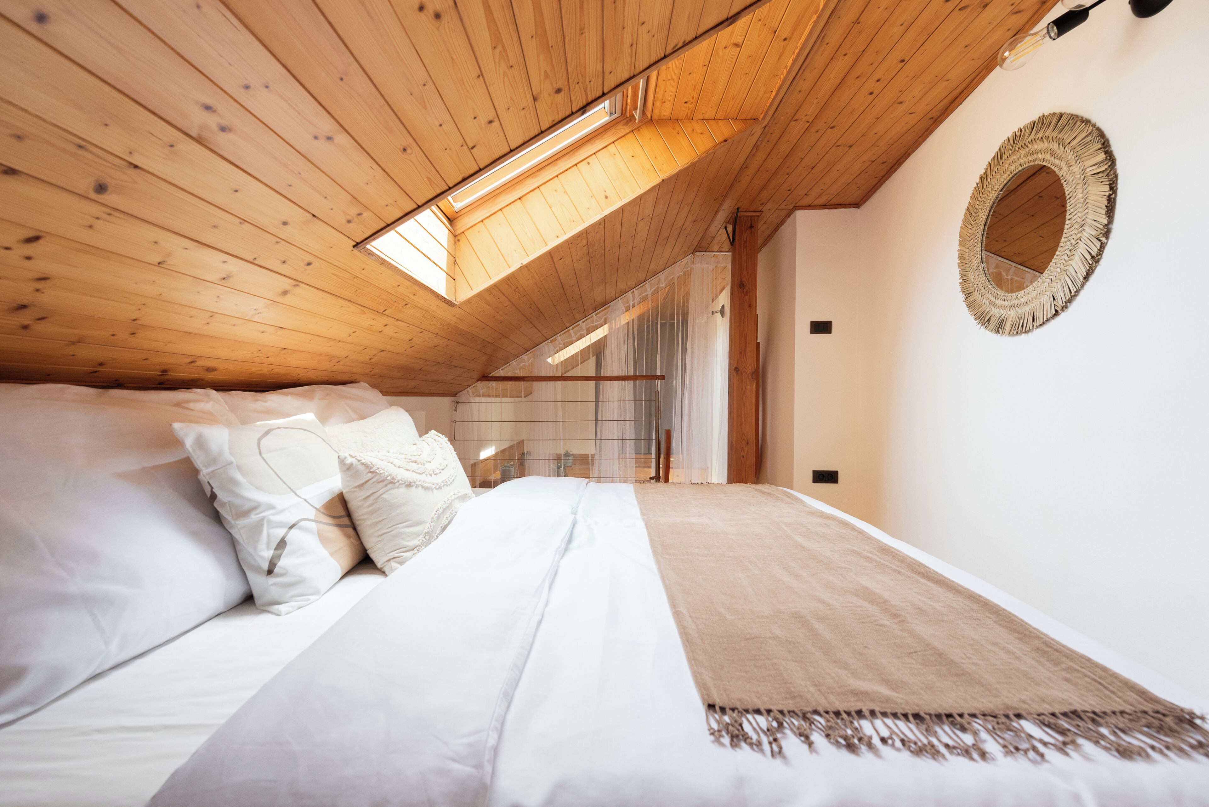 A bedroom with a sloped ceiling, a large bed with white linens, a woven wall hanging, and a skylight.