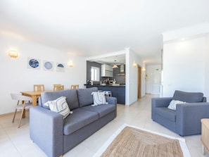 A modern living room with a grey sofa set, a dining table with chairs, and a kitchen in the background. - Villa Louisa - Garden Villa, Carvoeiro (Carvoeiro)
