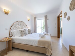 A bedroom with a large bed, bedside tables, a window with curtains, and a view of the outdoors. - Villa Louisa - Garden Villa, Carvoeiro (Carvoeiro)