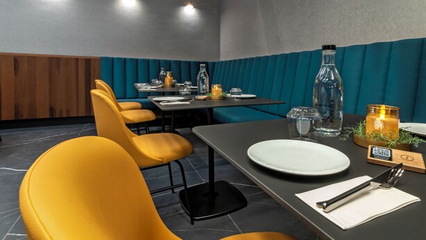 A restaurant interior with yellow chairs, a table set for dining, and a teal-colored wall.