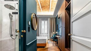 A hotel room with a shower, a bed, a desk, and a view of the sky through a skylight.