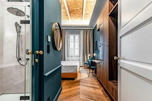 A hotel room with a shower, a bed, a desk, and a view of the sky through a skylight.