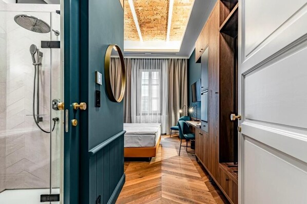 A hotel room with a shower, a bed, a desk, and a view of the sky through a skylight.