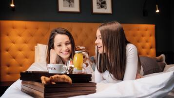 A room with a tufted headboard, a bedside table with a tray containing a cup, a glass of juice, and a pastry.