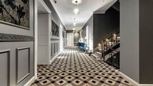 A hallway with a checkered floor, a staircase with a metal railing, and a ceiling light fixture.