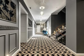 A hallway with a checkered floor, a staircase with a metal railing, and a ceiling light fixture.