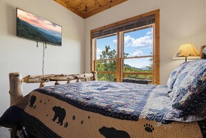Ein Schlafzimmer mit einem großen Bett, einem hölzernen Kopfteil, einem Fenster mit Blick ins Grüne und einem Gemälde an der Wand.