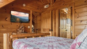 A wooden cabin interior with a bed, a mounted television, and a wooden door. - New Listing, Game Room, Theater Room, Free Attractions (Sevierville)