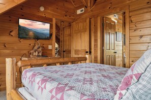 Ein Holzblockhaus-Innenraum mit einem Bett, einem an der Wand befestigten Fernseher und einer Holztür.