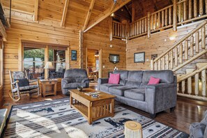 A wooden cabin interior with a gray sofa, wooden rocking chair, and a staircase. - New Listing, Game Room, Theater Room, Free Attractions (Sevierville)