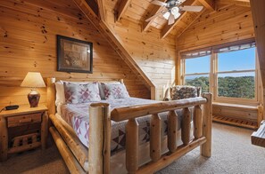 Ein Schlafzimmer in einer Holzhütte mit einem Bett, einem Nachttisch, einer Lampe, einem Bilderrahmen und einem Fenster mit Aussicht.
