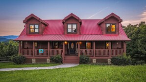 A log cabin with a red metal roof, two chimneys, and a porch with railings. - New Listing, Game Room, Theater Room, Free Attractions (Sevierville)