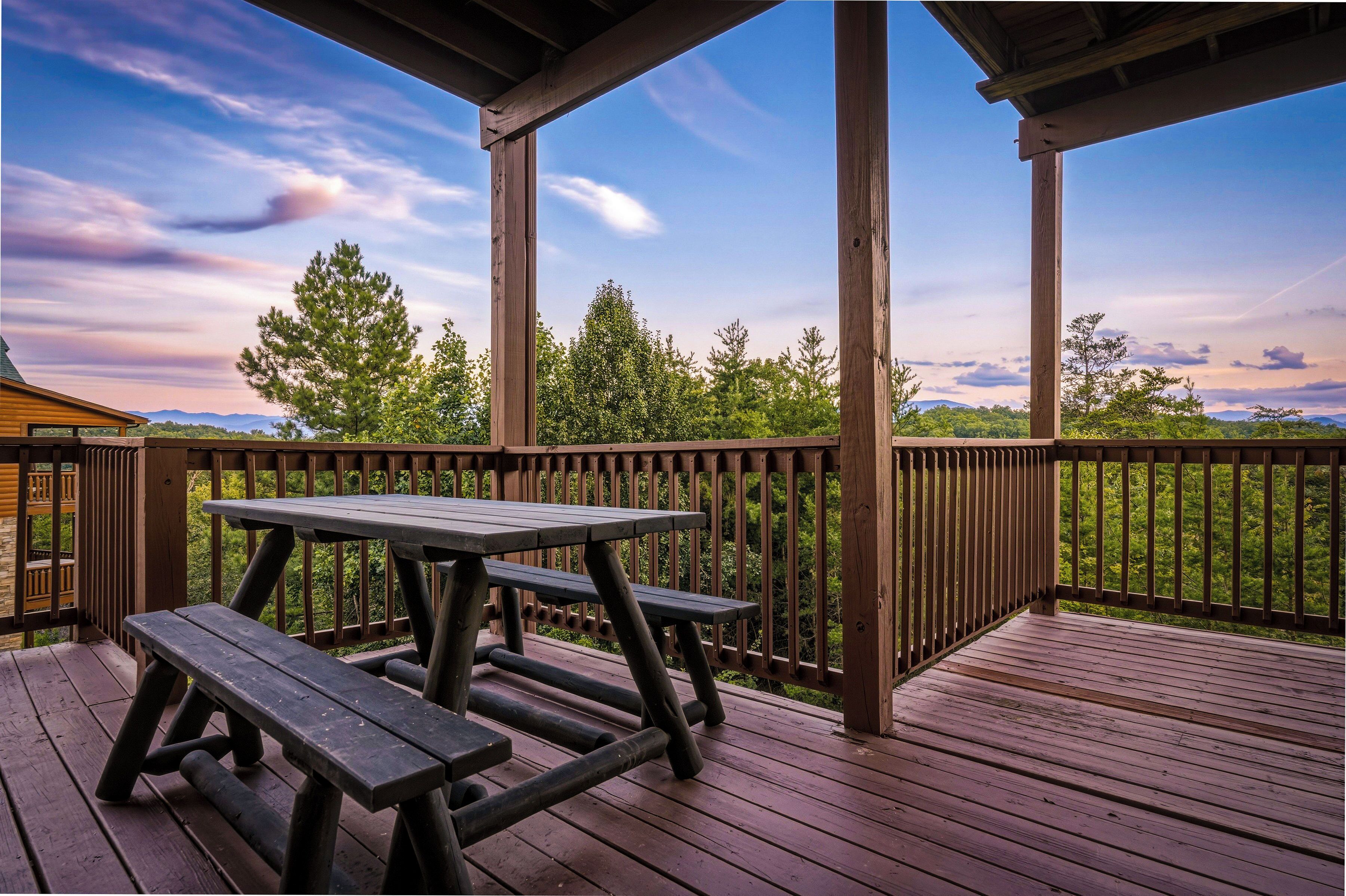 A wooden deck with picnic tables and a railing overlooking a forested landscape.