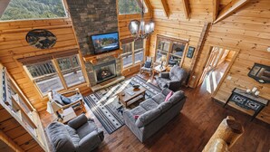 A cozy cabin interior with a fireplace, comfortable seating, and large windows offering views of the outdoors. - New Listing, Game Room, Theater Room, Free Attractions (Sevierville)