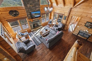 Ein gemütliches Blockhaus-Interieur mit Kamin, bequemen Sitzgelegenheiten und großen Fenstern mit Blick ins Freie.