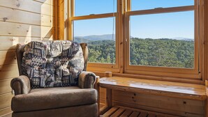 A wooden cabin interior with a cushioned chair facing a large window overlooking a forested mountain range. - New Listing, Game Room, Theater Room, Free Attractions (Sevierville)