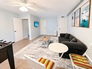 A living room with a sofa, a coffee table, a TV, and a futsal table. - Luxury Retreat Near Indian Rocks Beach Pool • Game Room • Sleeps 8+ (Seminole)