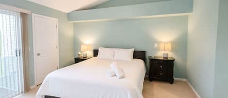 Quarto com cama, duas mesinhas de cabeceira, ventilador de teto e uma porta.
