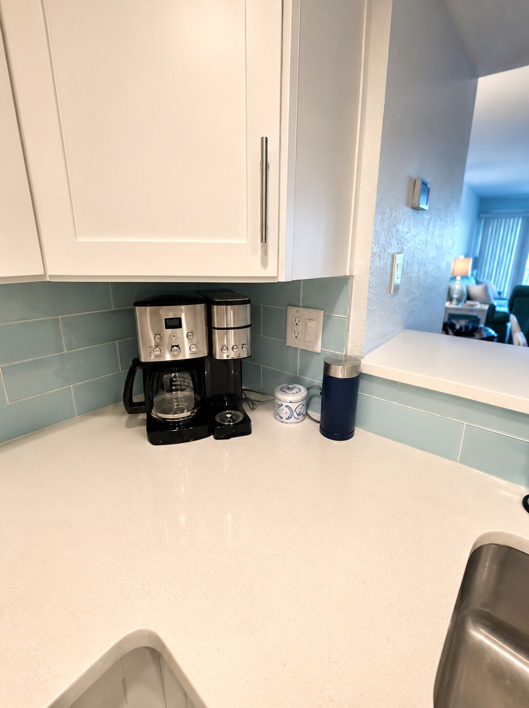 A kitchen with white cabinets, a coffee maker, a mug, and a small container.