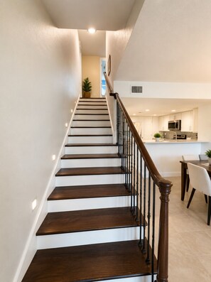 A staircase leading to a kitchen area with white walls and a wooden railing. - Luxury Retreat Near Indian Rocks Beach Pool • Game Room • Sleeps 8+ (Seminole)