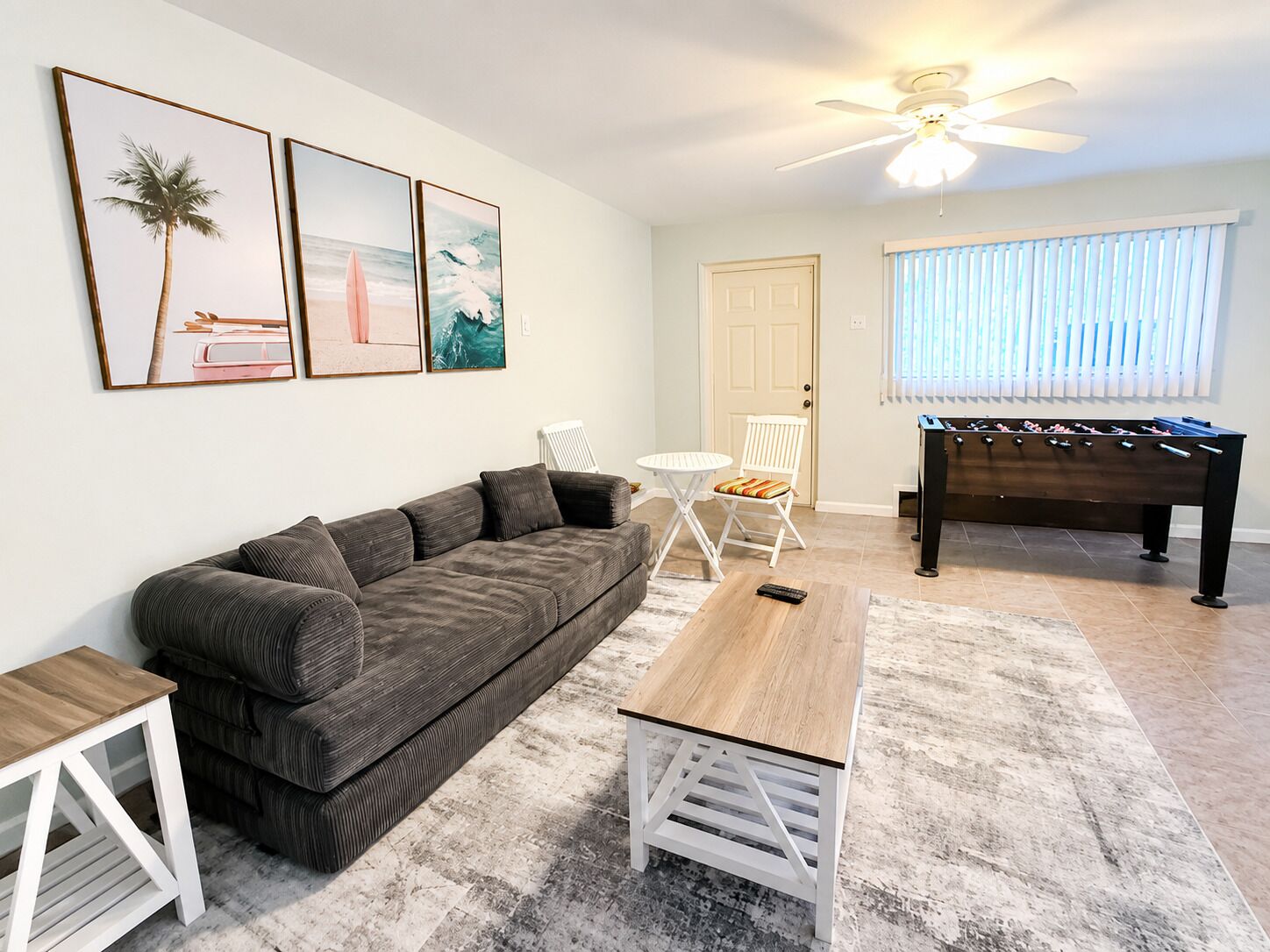 A living room with a sofa, coffee table, and a foosball table. There are three framed pictures on the wall.
