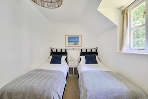 Ein Zimmer mit zwei Einzelbetten, einem Nachttisch mit Lampe, einem gerahmten Bild an der Wand und einem Fenster mit Vorhängen.