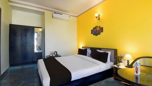 A hotel room with a bed, bedside table, lamp, and a small round table with a bottle. - Super Collection O Mall  (Jaipur)