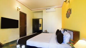 A hotel room with a bed, a flat-screen TV, a wall-mounted air conditioner, and a small table with a lamp and a vase of flowers. - Super Collection O Mall  (Jaipur)