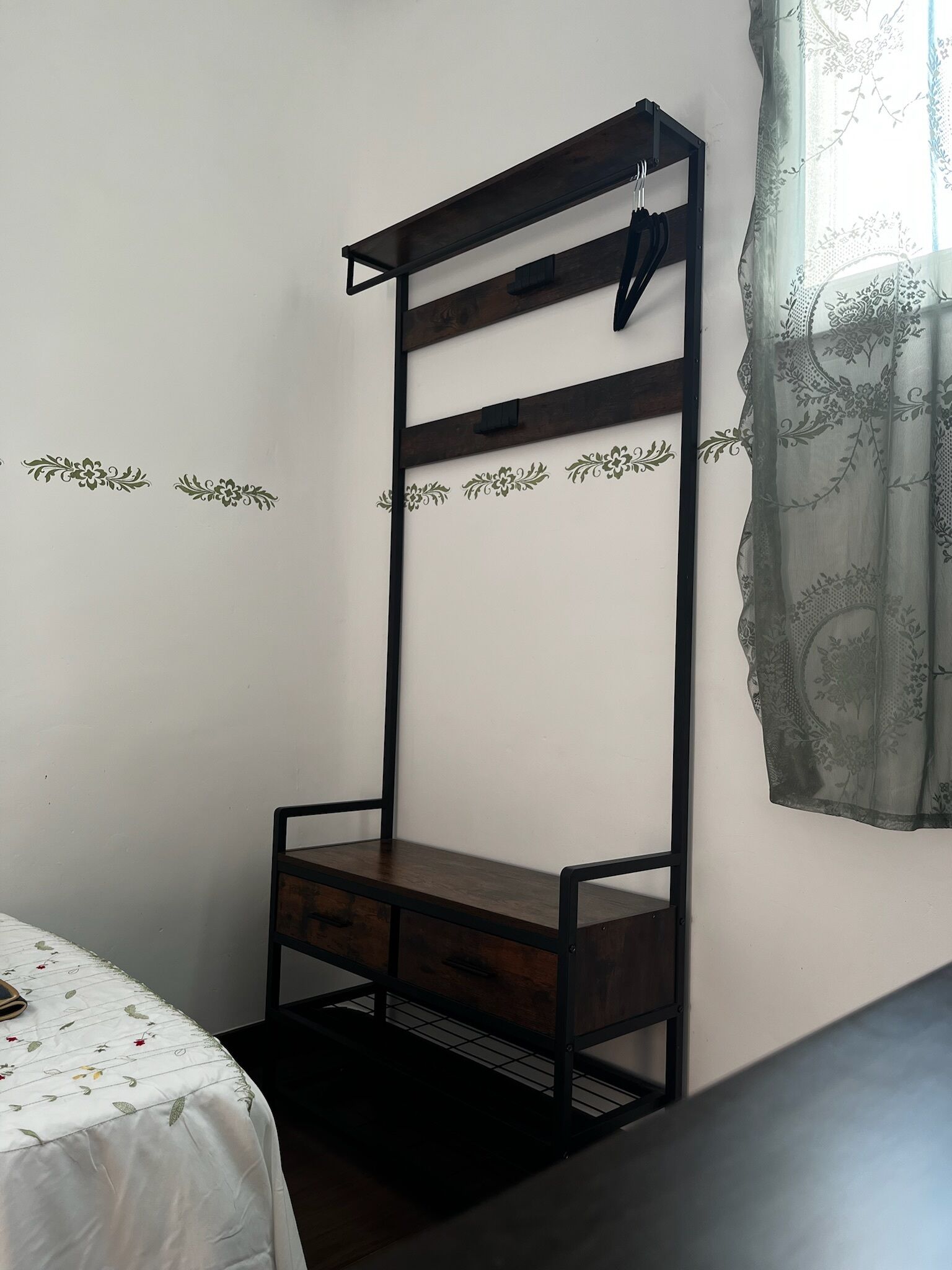 Een stapelbed met houten frame en metalen leuningen, een klein bureau met lades, en een bed met bloemenprint beddegoed.