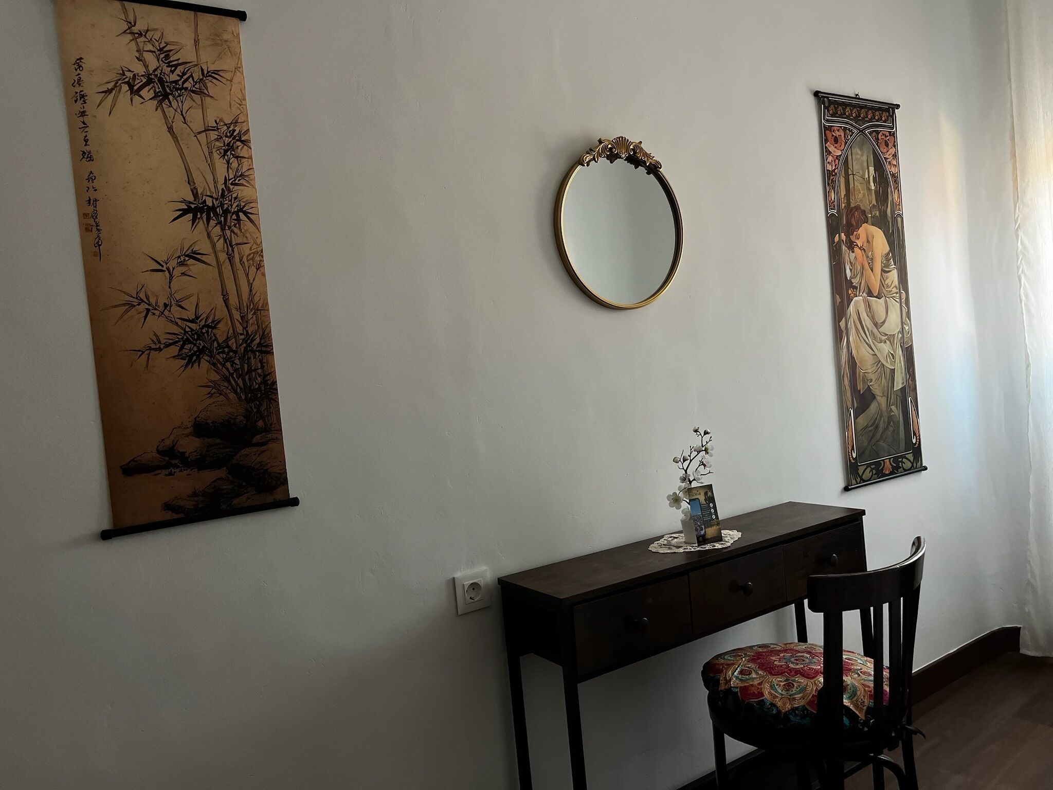 Una habitación con escritorio, silla, espejo en la pared y dos cuadros enmarcados.