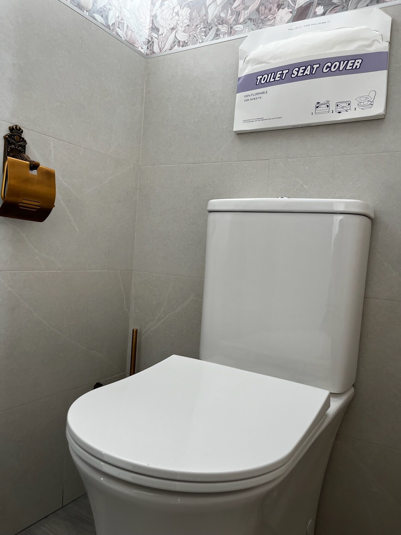 Inodoro con tapa en la pared, un dispensador de papel higiénico y un escobón.