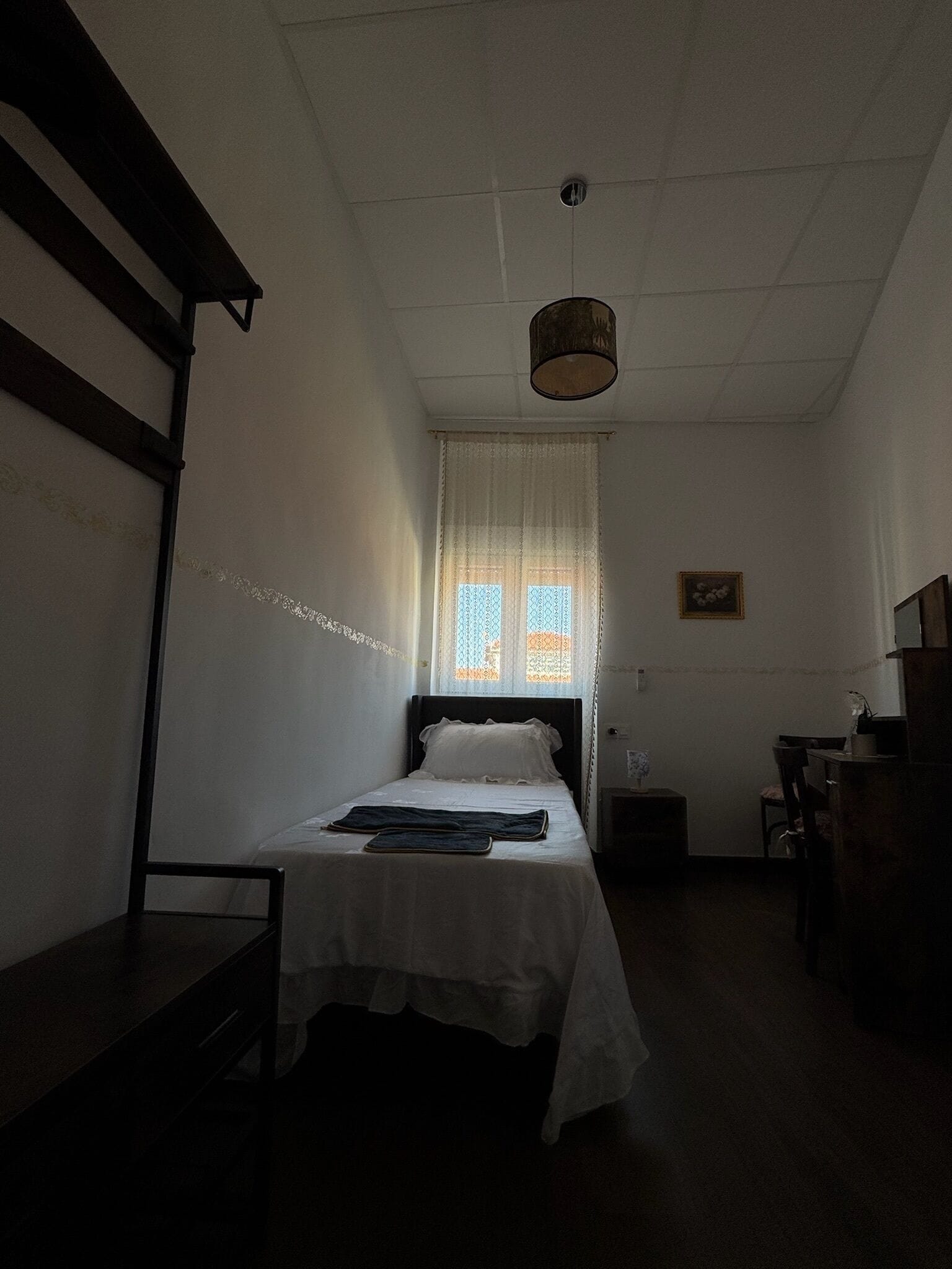 A dimly lit room with a single bed, a small table, and a chair.