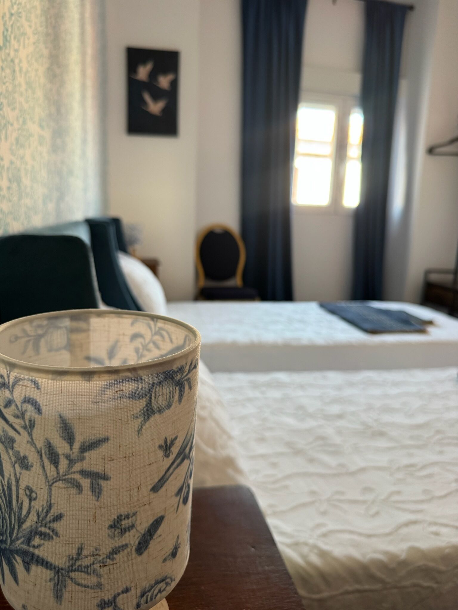 A bed with a white bedspread, a dark green headboard, and a small wooden chair in a room with a window and curtains.