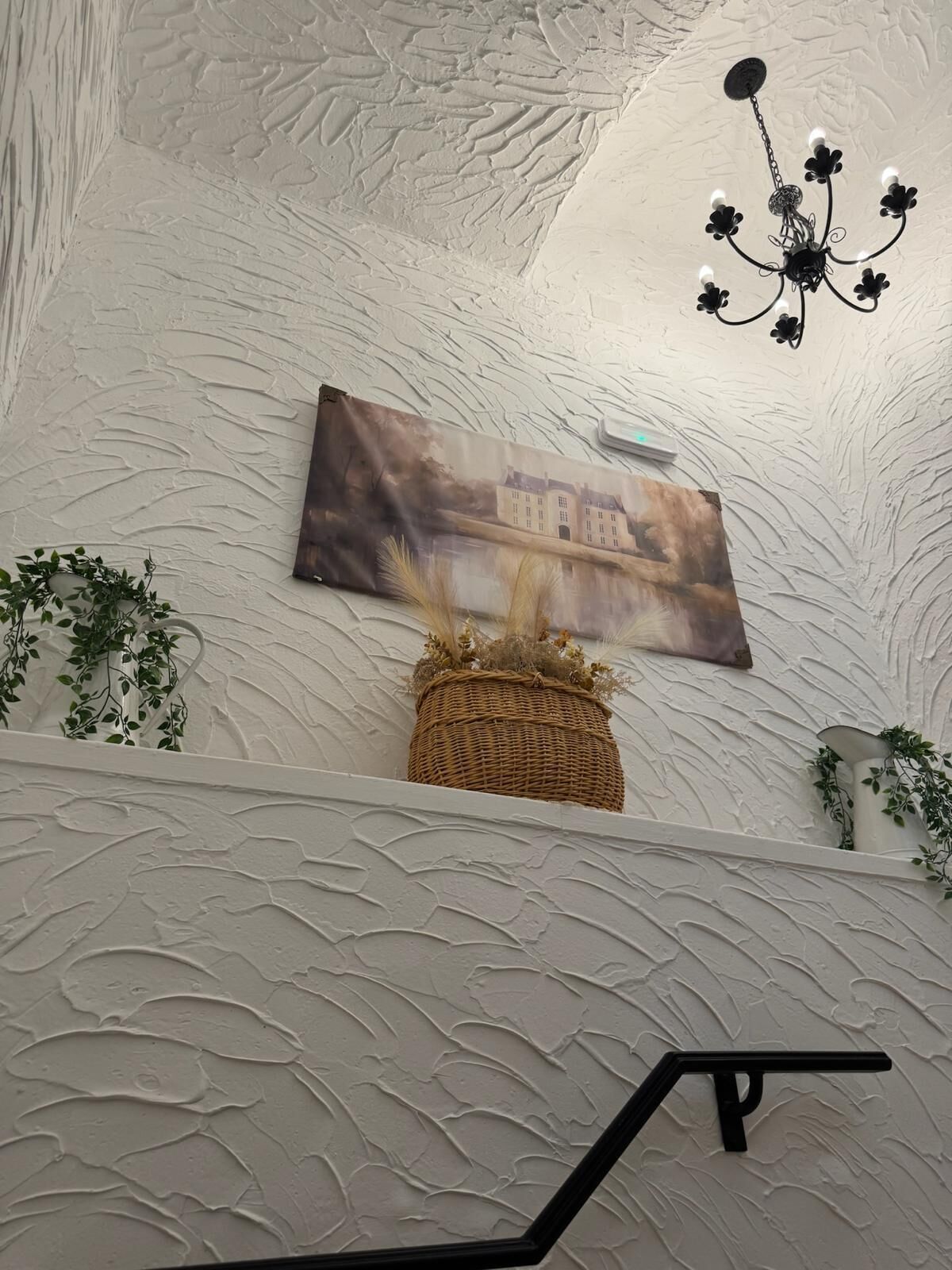 Pared texturizada con un marco de fotos, una cesta tejida y una barandilla de metal negro.