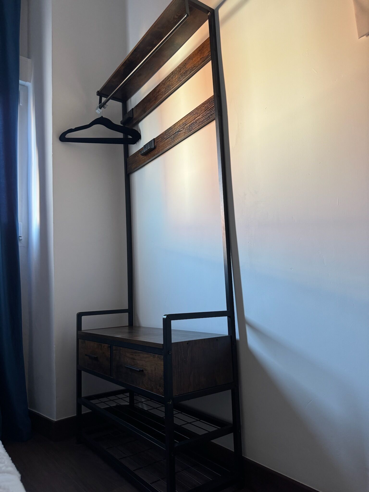 Una cama litera con estructura de madera y barandillas metálicas, un perchero negro colgando y una pared blanca al fondo.