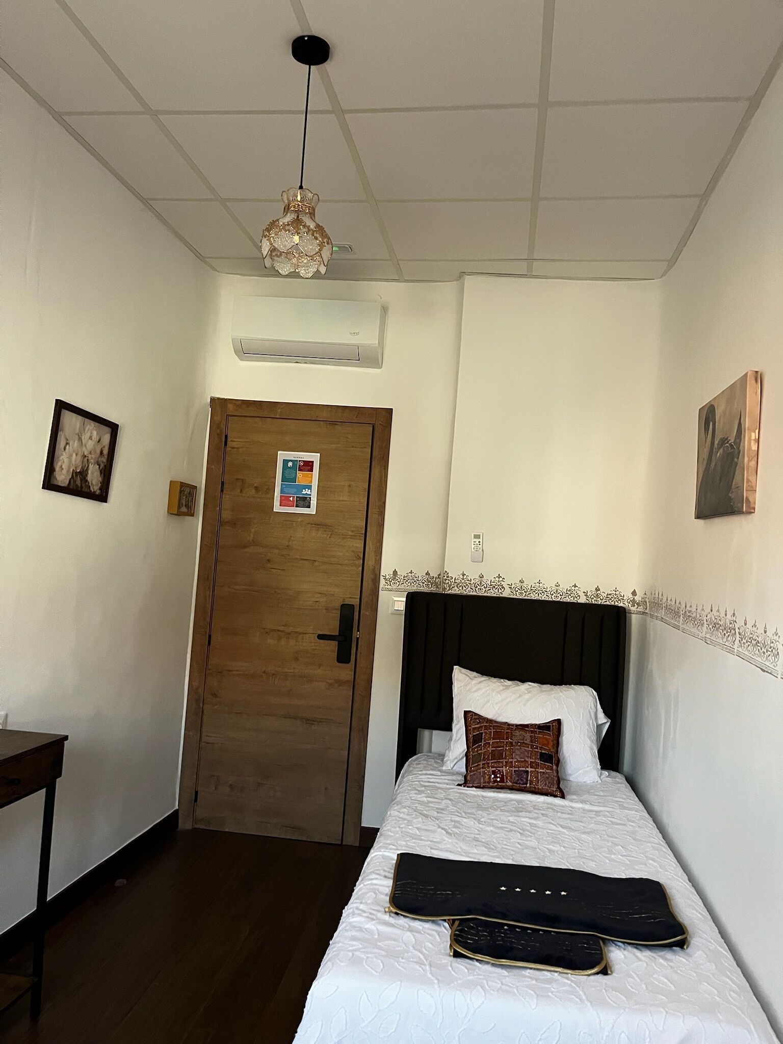 A hotel room with a bed, a desk, a door, and a ceiling light fixture.