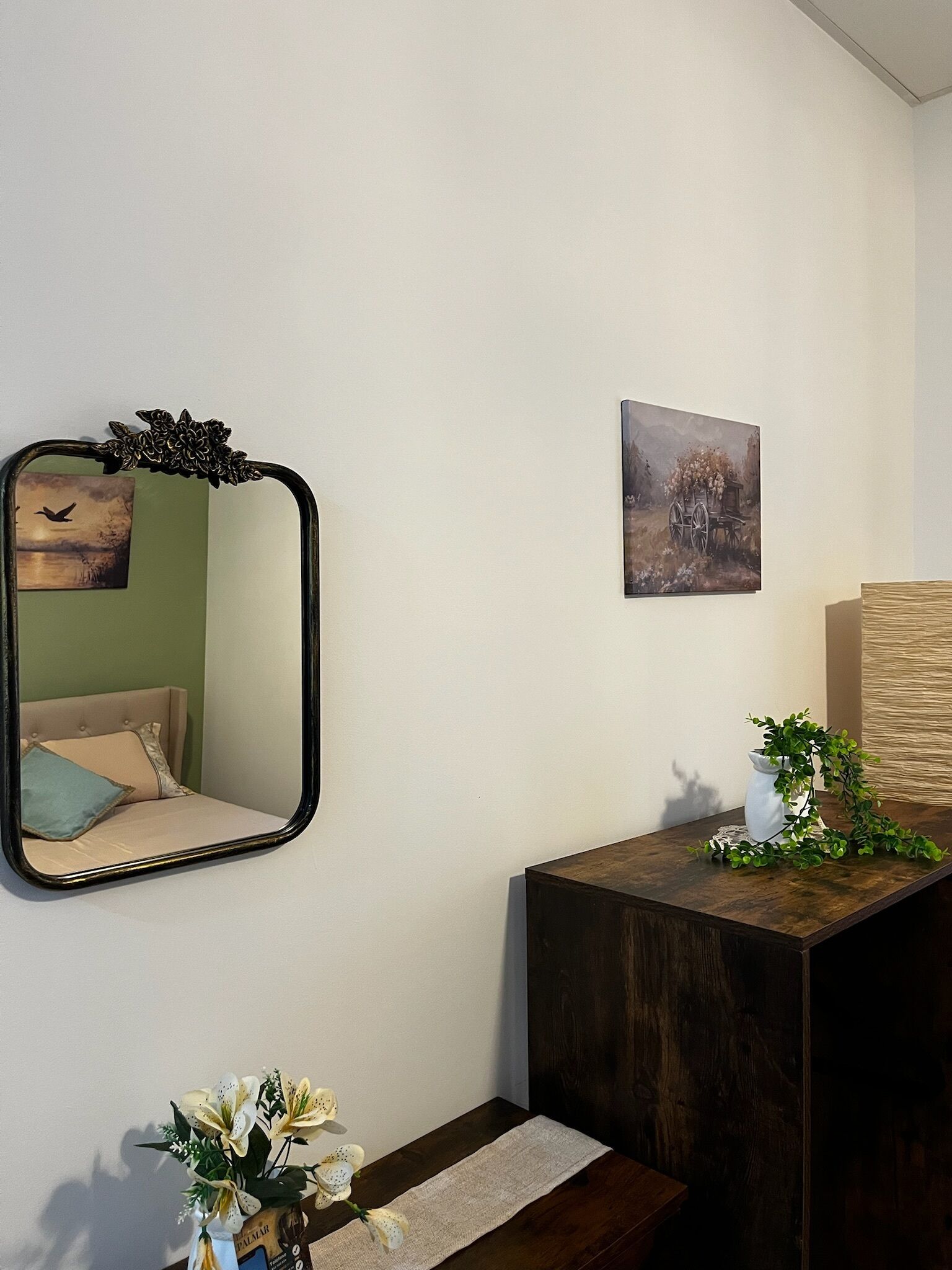 Una habitación con un espejo, un cuadro, una planta y una mesita.