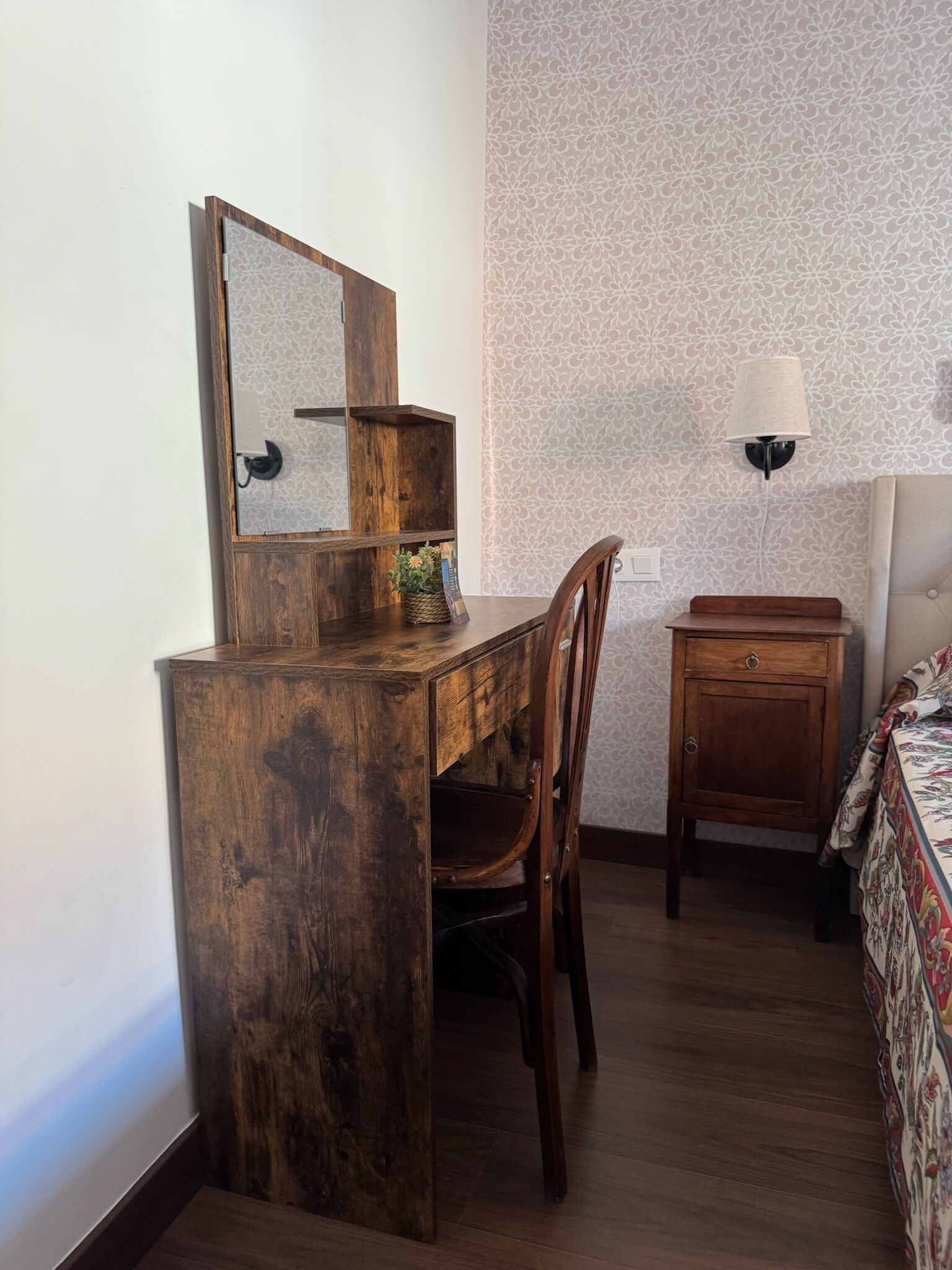 Un bureau en bois avec un miroir, une chaise, un petit meuble et une lampe.