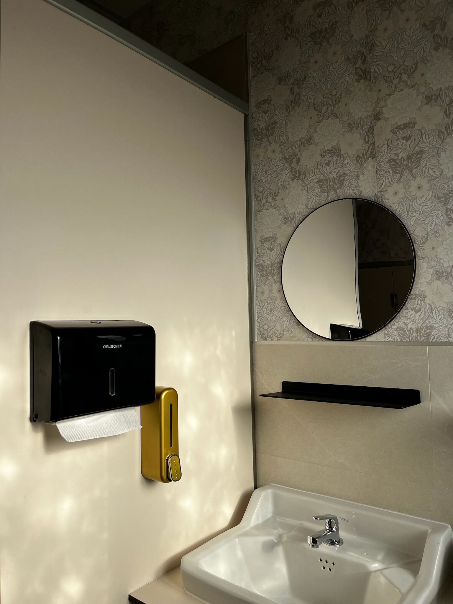 Un baño con dispensador de jabón en la pared, un espejo y un lavabo.