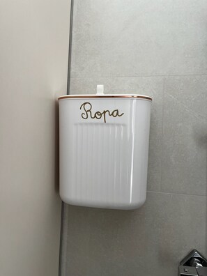 Un recipiente de cerámica blanca con la palabra 'Ropa' grabada, colocado en una pared de azulejos.