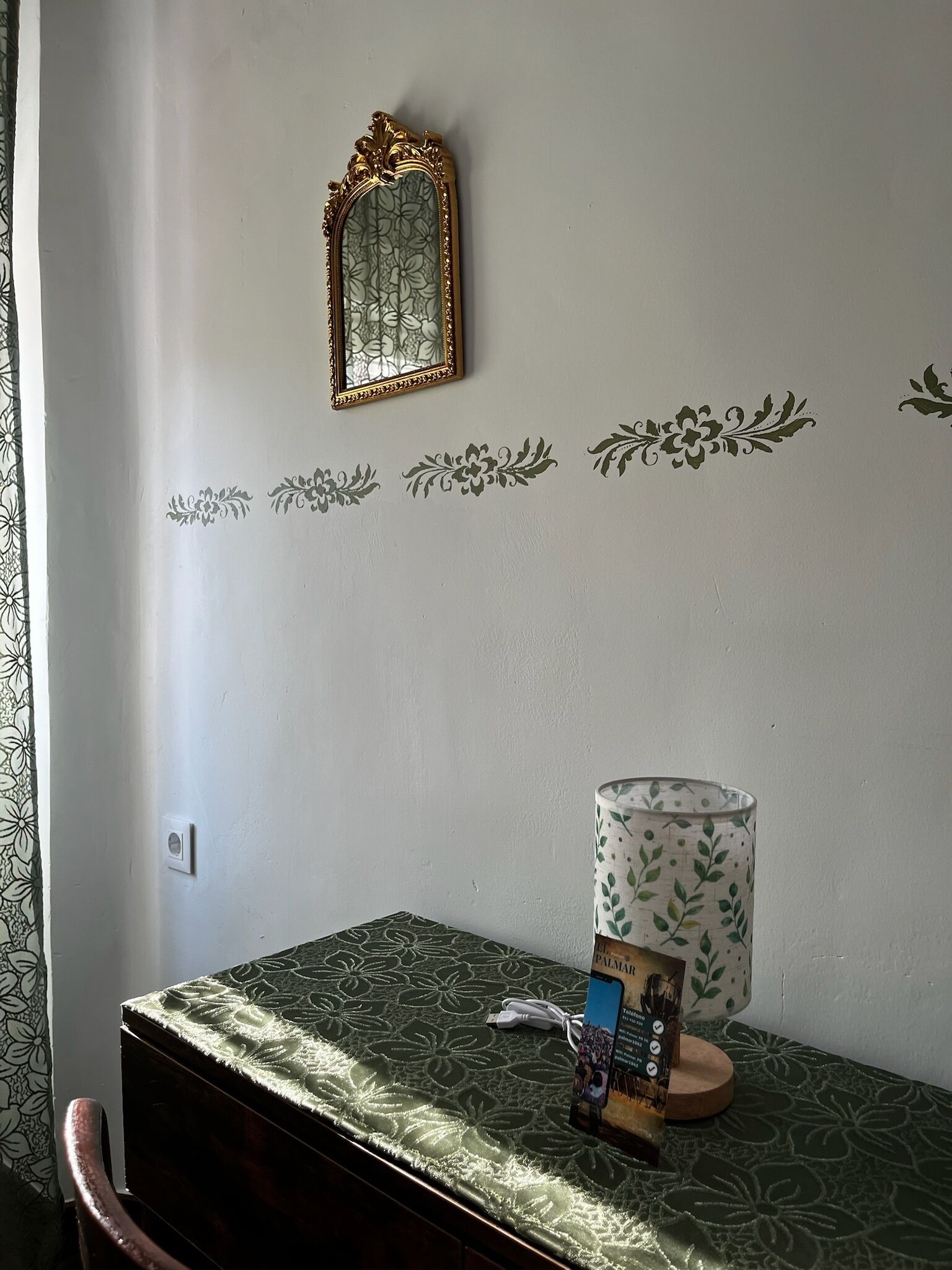 A room with a bed, a bedside table, a lamp, a framed mirror, and decorative wall stickers.