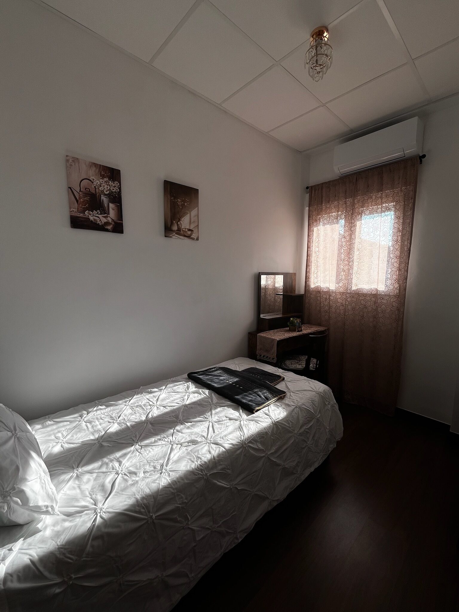 Een slaapkamer met een bed, een nachtkastje, een spiegel en twee aan de muur bevestigde schilderijen.