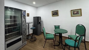 A room with a refrigerator, a vending machine, a glass partition, and a table with chairs. - Pensión El Palmar  (Tobarra)