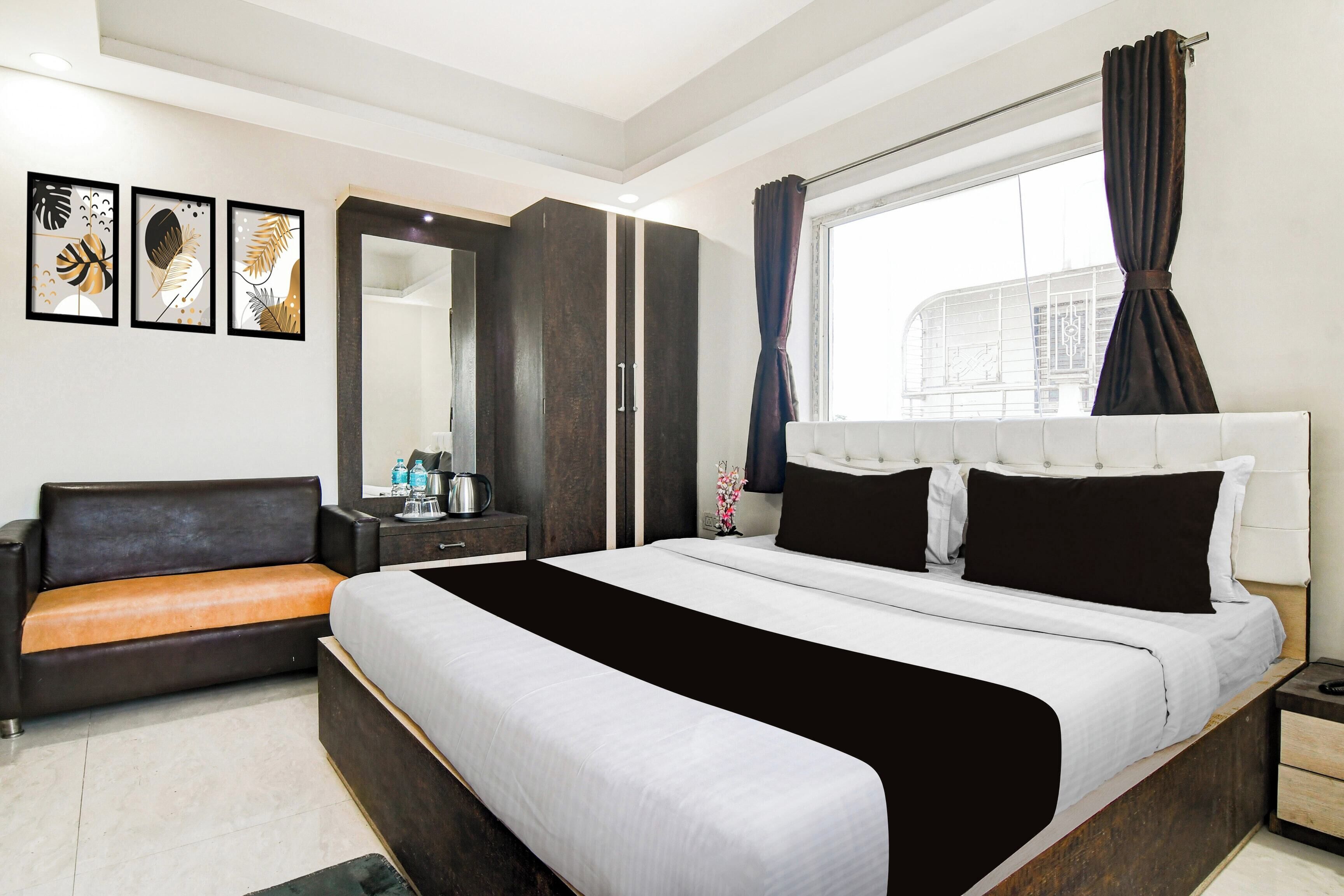 A modern hotel room with a bed, a sofa, a dresser, a mirror, and artwork on the wall.