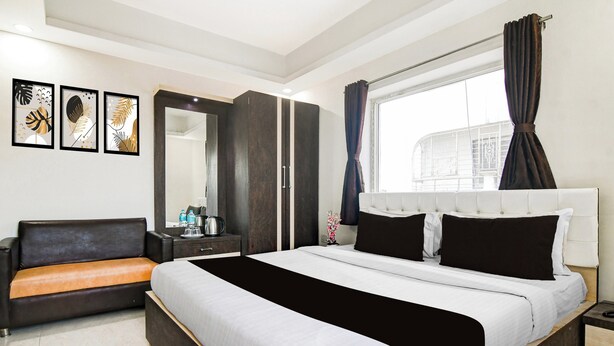 A modern hotel room with a bed, a sofa, a dresser, a mirror, and artwork on the wall. - Super Collection O City Center 2 (Barasat)