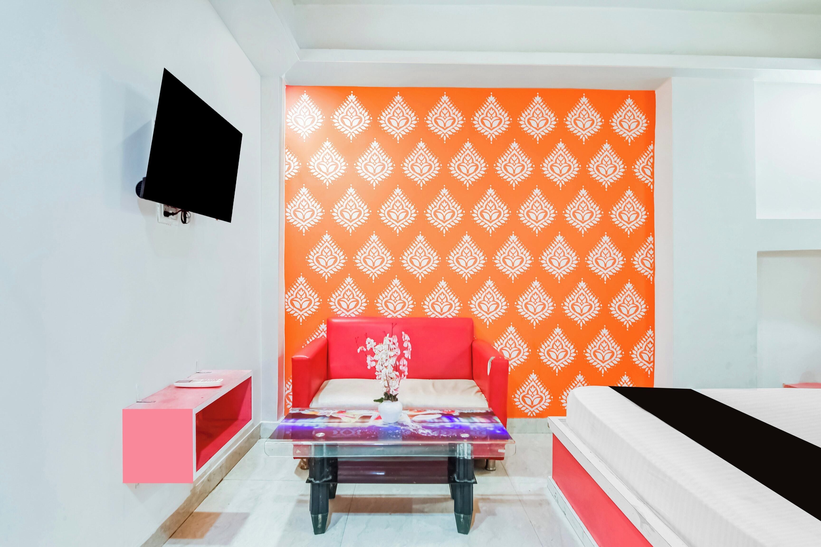 A hotel room with a red sofa, a glass coffee table, and a patterned orange wall.