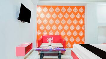 A hotel room with a red sofa, a glass coffee table, and a patterned orange wall.