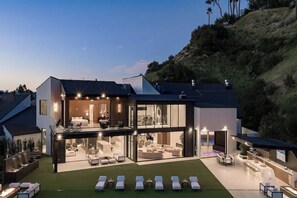 A modern two-story house with a large open-plan living area, a separate bedroom, and a well-lit outdoor patio with lounge chairs. - Lemmer Estate - Tarzana Golf Course Home with Indoor Pool (Tarzana)